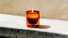 A 6 oz Double Wall Candle lit on a cement surface. 
