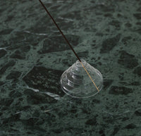 The Clear Glass Meso Incense Holder on a green marble surface. 