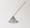 The Gray Glass Meso Incense Holder with an incense in it on a grayish background.