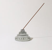 The Gray Glass Meso Incense Holder with an incense in it on a grayish background.