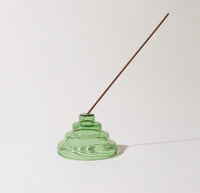 The Verde Glass Meso Incense Holder with a incense in it on a grayish background.