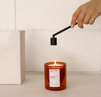 A hand holding the Candle Snuffer above the Castillo Double Wall Candle on a cream background. 