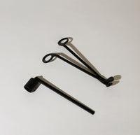 The Candle Snuffer next to the Candle Wick Trimmer on a grayish background.