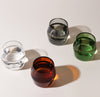 Top view of the Amber, Clear, Gray and Verde 6 oz Century Glasses filled with water on a cream background.