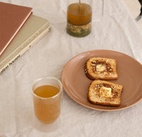 A 12 oz Clear Double Wall Glasses filled with tea next to a plate of toast.