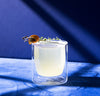 A 6 oz Clear Double Wall Glasses with a cocktail on a blue background. 