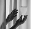 A black and white image of hands holding a 6 oz Clear Double Wall Glass.  