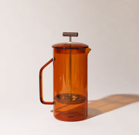 A Amber Glass French Press on a cream background.