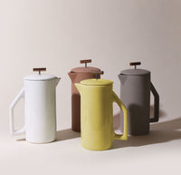 A Chartreuse Ceramic French Press with A Gloss Cream, A Matte Sand and A Matte Gray Ceramic French Press behind it.