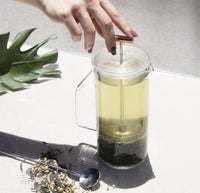 An overhead shot of the Clear Glass French Press filled with green tea on a grayish background. 