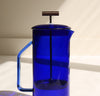 A close up side view of a Cobalt Glass French Press on a cream background.
