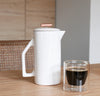 A Gloss Cream Ceramic French Press and a Clear Double Wall Glass filled with Coffee on a wooden table. 