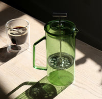 A Verde Glass French Press on a table with a double wall glass filled with coffee on the side.