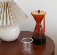 The Amber Pour Over Carafe filled with coffee and a Clear Double wall Glass on a wooden surface. 