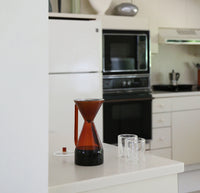 The Amber Pour Over Carafe filled with coffee and two Clear Double wall Glass on a kitchen countertop.