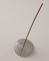 A top view of the Gray Glass Meso Incense Holder with an incense stick, on a grayish background.