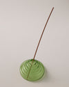 The Verde Glass Meso Incense Holder with an incense stick, on a grayish background.